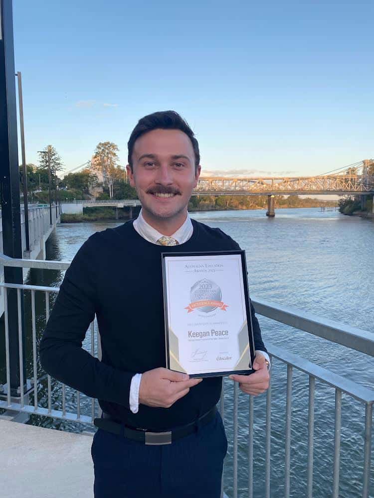 Keegan Peace proudly poses with his Australian Education Excellence Award nomination, with the lovely view of his local bridge. Images: Keegan Peace.