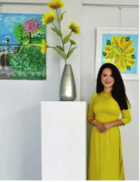 A person in a yellow dress standing next to a vase with flowers

Description automatically generated